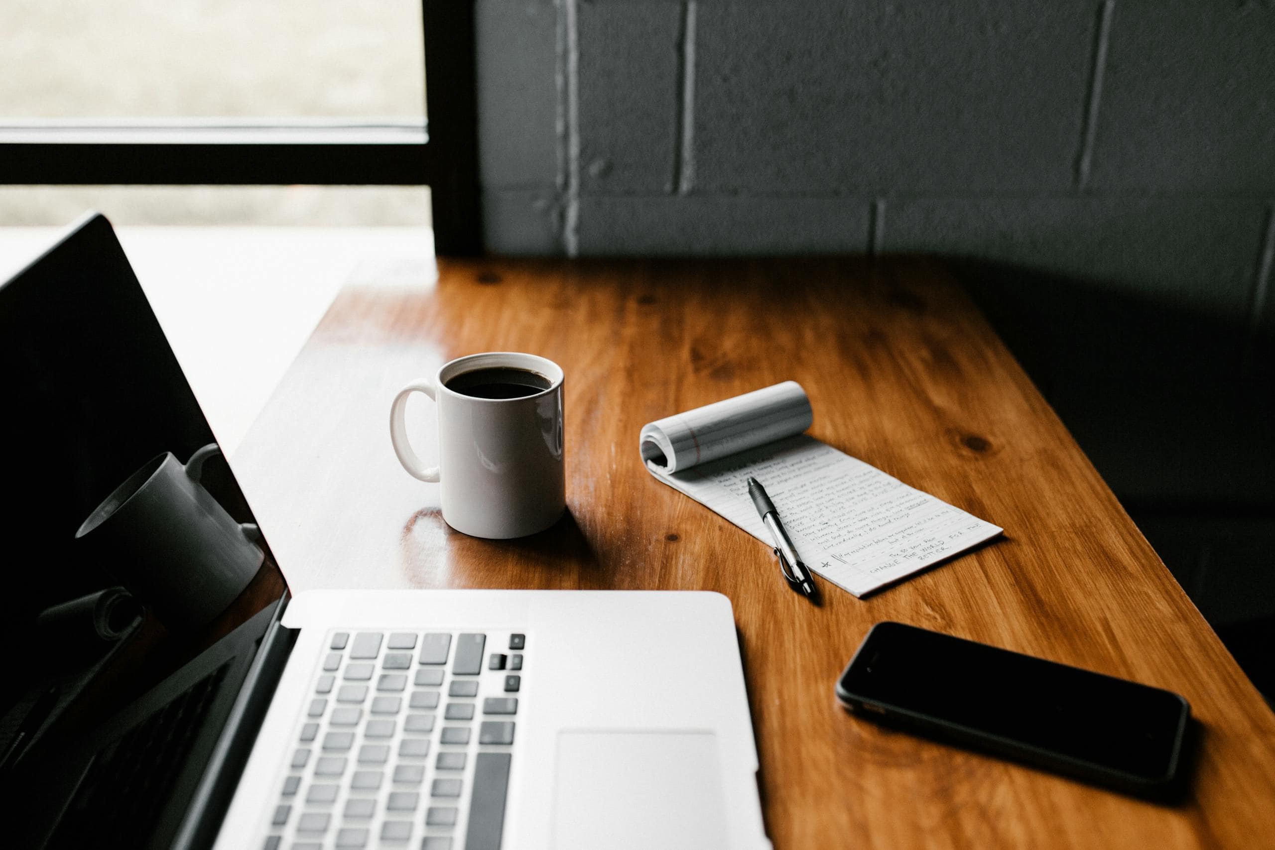 A tidy workspace featuring a laptop, coffee cup, phone, and notepad on a wooden desk for Director Reports and Audits