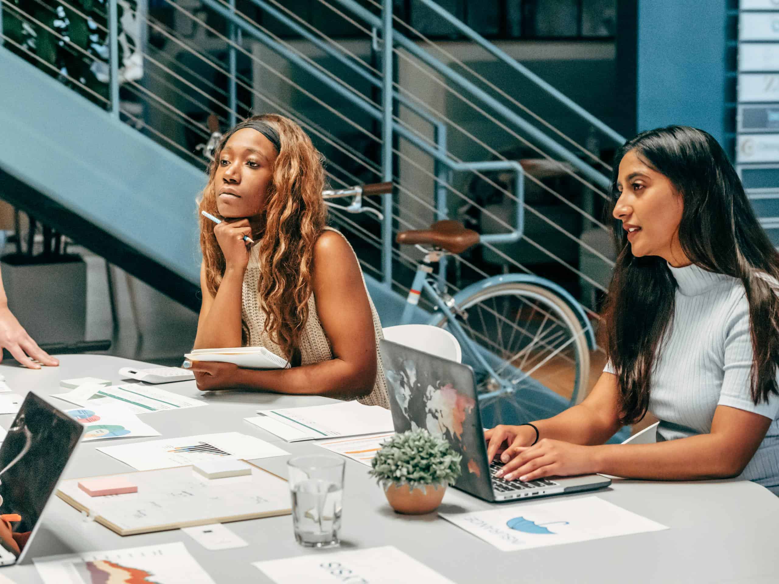 Diverse women engaging in a collaborative meeting at an office desk, focused on planning and innovation with tax forecasting