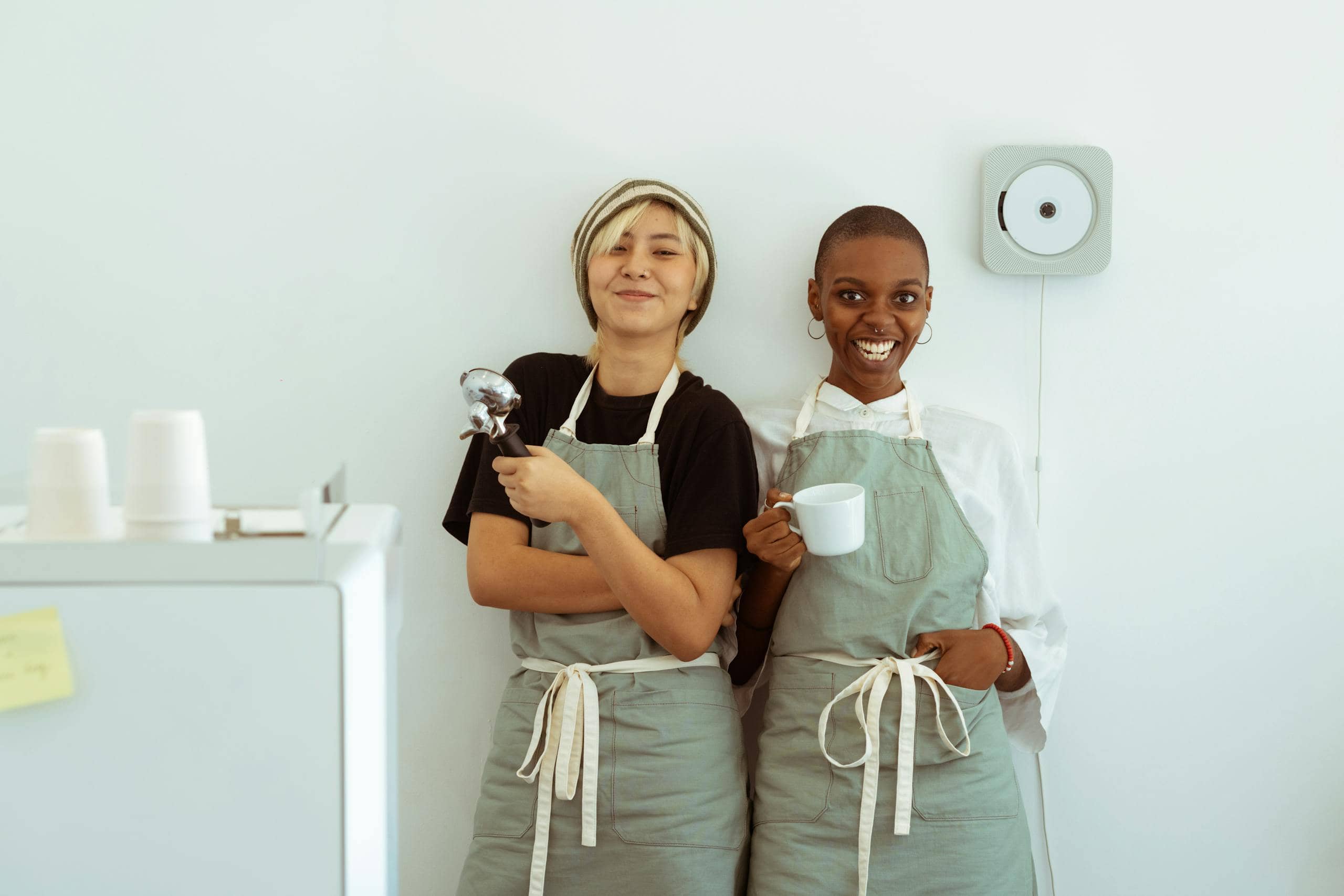 Two cheerful baristas in aprons holding coffee in a modern cafe setting.